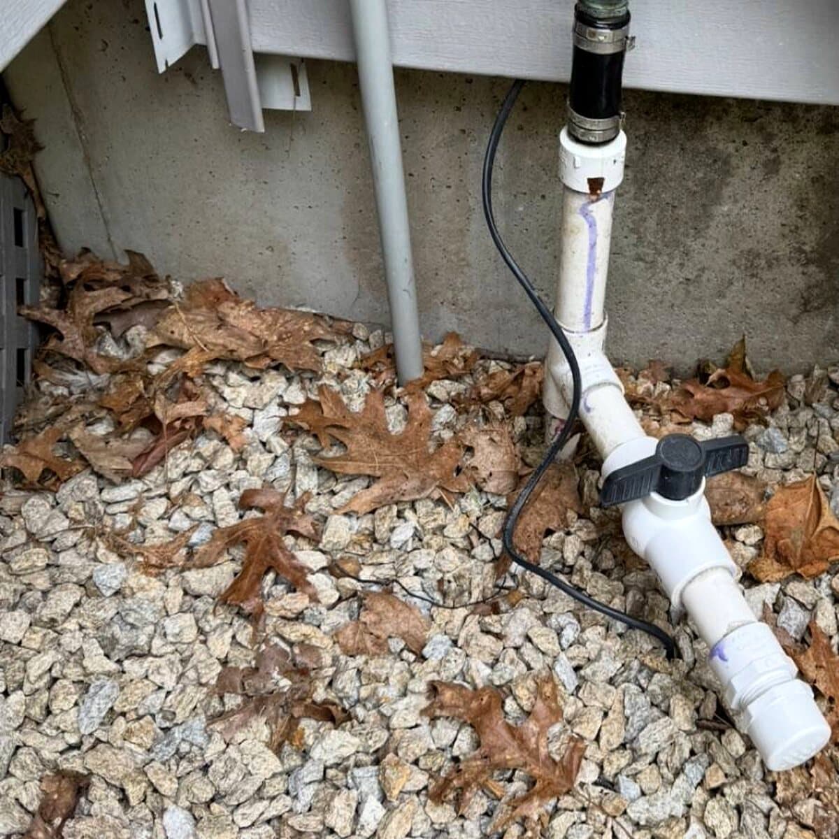 Exterior PVC pipework and valve beside a foundation